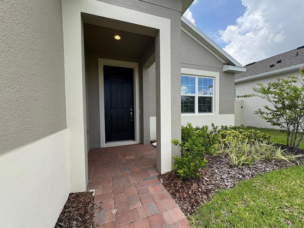 A brick walkway leads to the covered entryway of a house with a black door — 366 SIWTCHGRASS LOOP, CLERMONT, FL