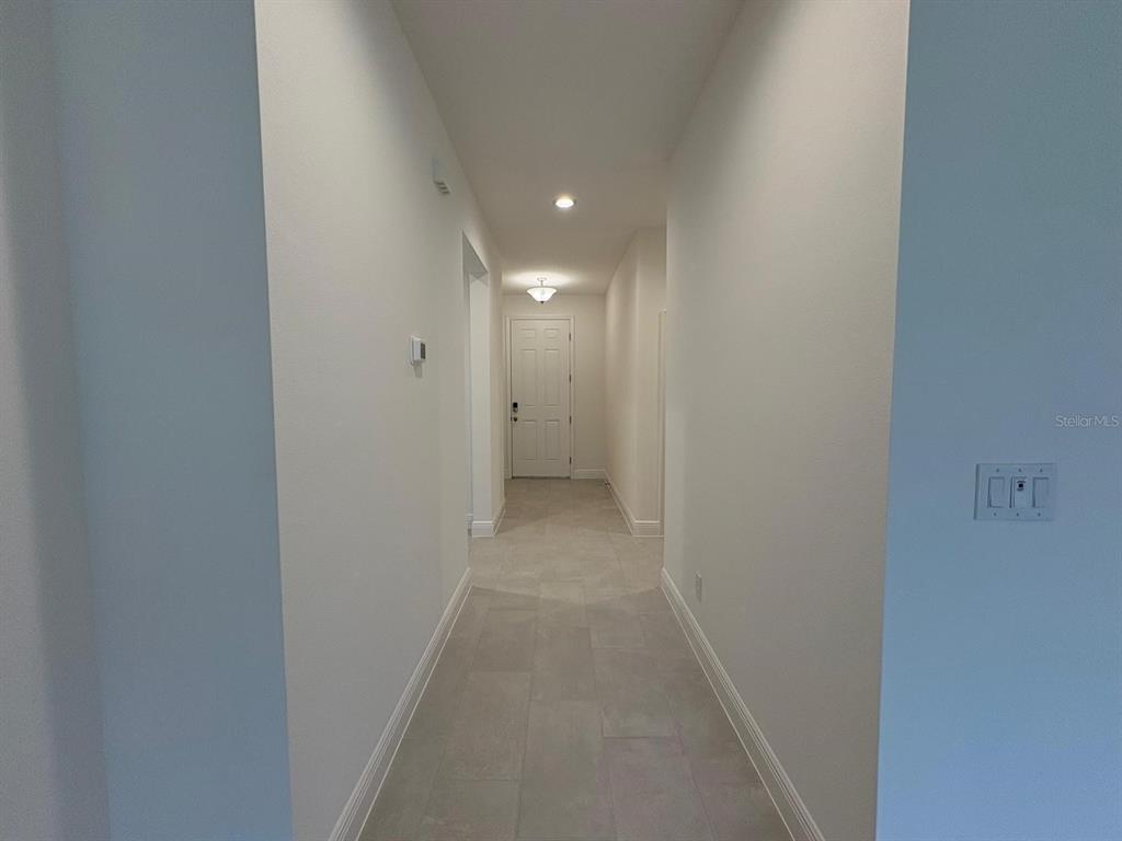 A long, narrow hallway with light-colored tile flooring leads to a white door — 366 SIWTCHGRASS LOOP, CLERMONT, FL