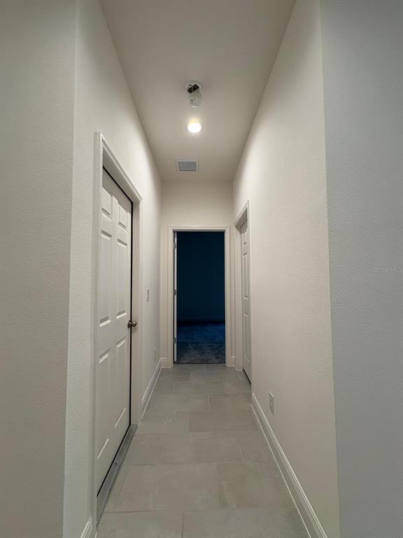 A narrow hallway with light-colored tile flooring leads to a doorway into a dark room — 366 SIWTCHGRASS LOOP, CLERMONT, FL