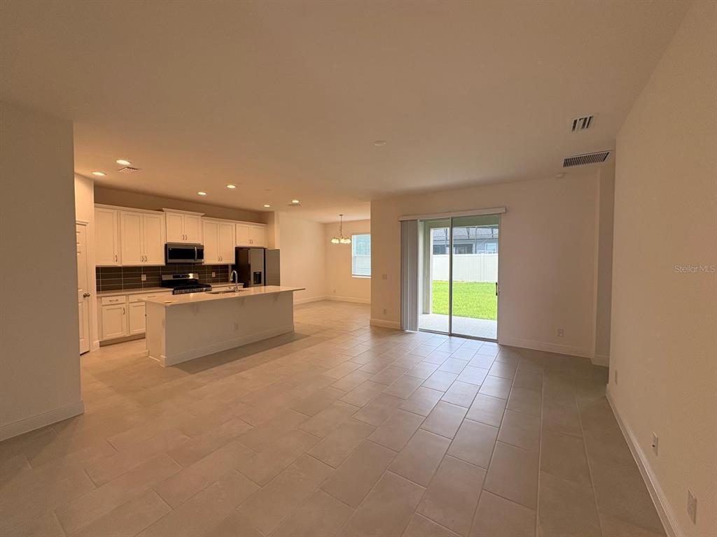 An open-concept kitchen with white cabinetry and an island overlooks a tiled living area — 366 SIWTCHGRASS LOOP, CLERMONT, FL