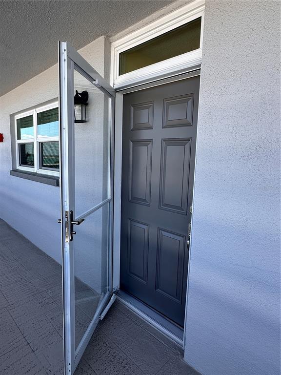 A gray front door with a glass storm door is set in a stucco wall — 5900 SHORE BOULEVARD S UNIT 504, GULFPORT, FL