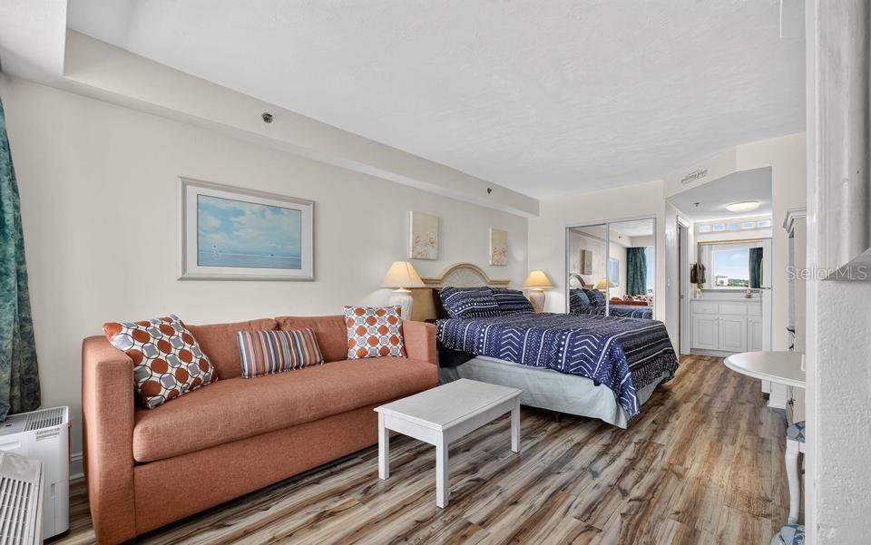 A bedroom features a sofa, a bed with a blue patterned quilt, and wood flooring — 2700 N ATLANTIC AVENUE UNIT 507, DAYTONA BEACH, FL