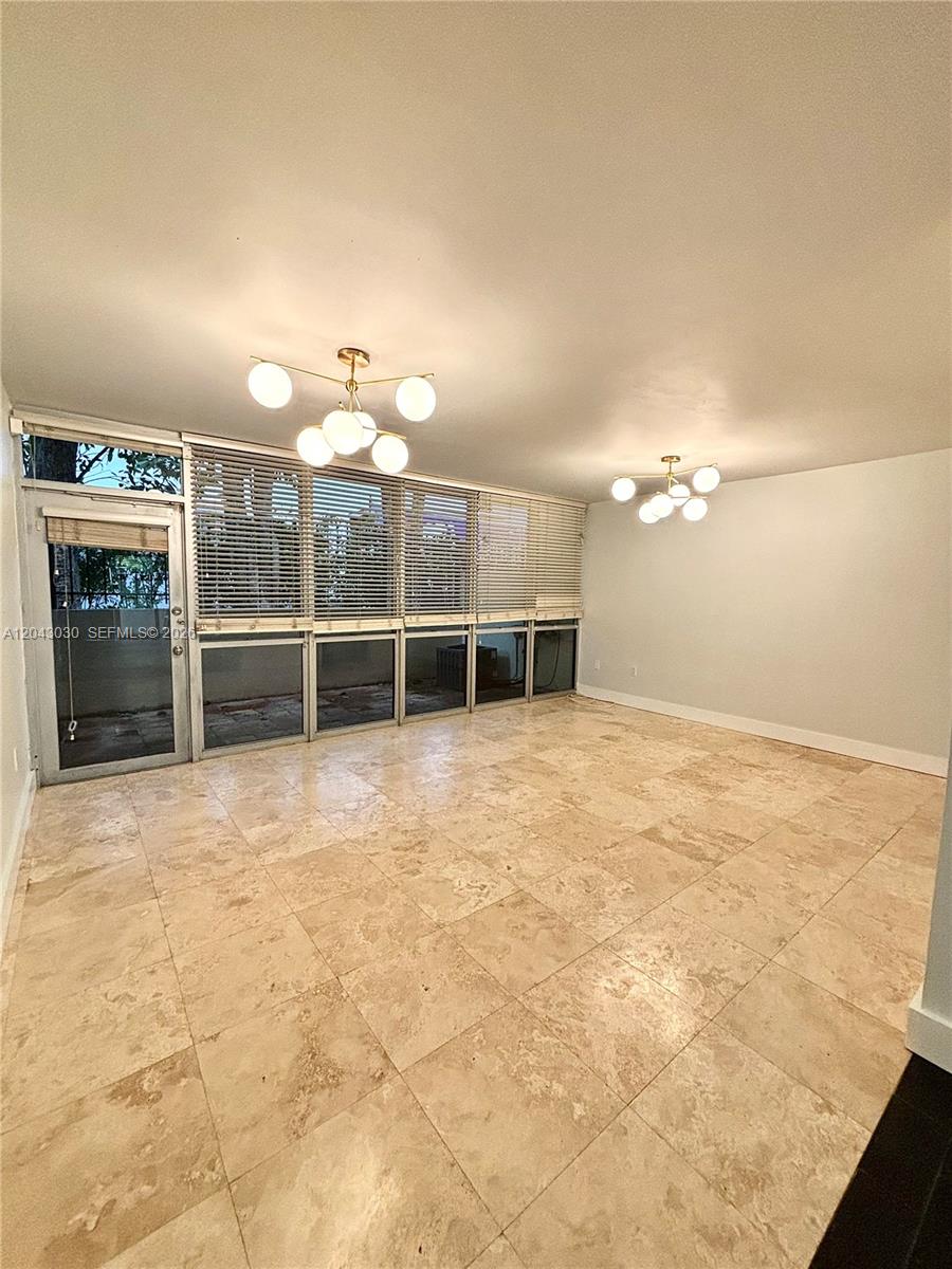 An empty room features light-colored tile flooring, two modern chandeliers, and large glass sliding doors — 2666 Tigertail Ave # 114, Miami FL 33133, MIAMI, FL