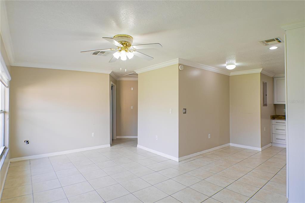 A living room with beige walls, tile flooring, a ceiling fan, and an adjacent kitchen area — 21150 GERTRUDE AVENUE UNIT A3, PORT CHARLOTTE, FL