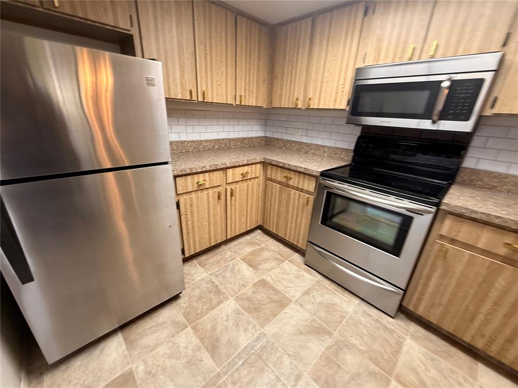 A kitchen features stainless steel appliances, wood cabinets, and a tiled floor — 12155 ENVIRONMENTAL DRIVE UNIT 6, NEW PORT RICHEY, FL