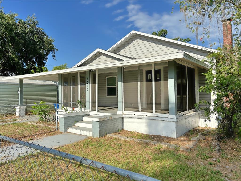 A single-story house with light gray siding, a screened-in front porch, and a brick chimney — 602 NW 1ST AVENUE, MULBERRY, FL