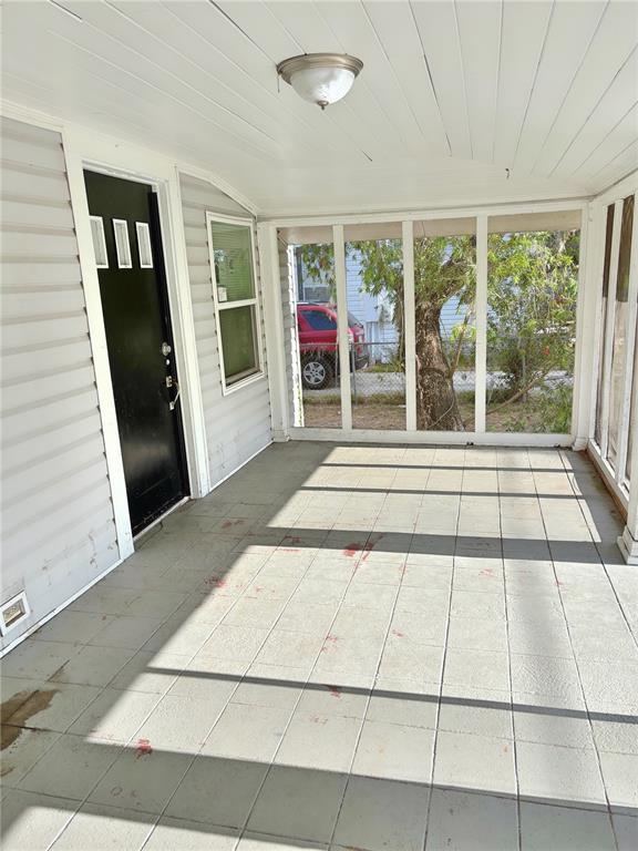 A covered porch with gray tiled flooring, a black front door, and screened-in walls — 602 NW 1ST AVENUE, MULBERRY, FL