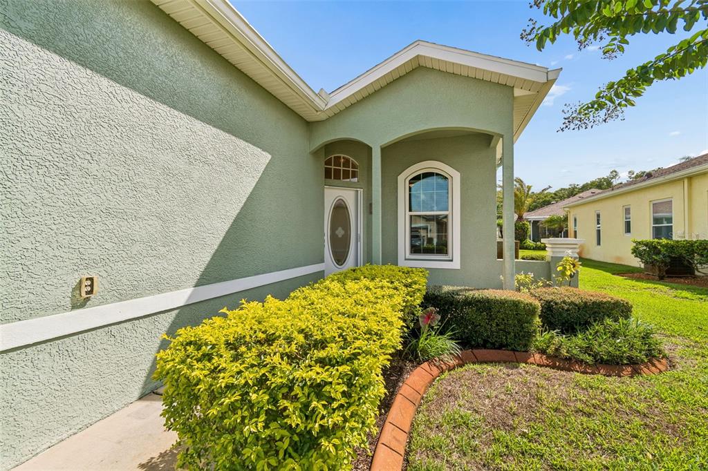 A green stucco house exterior features a covered entryway, a front door, and landscaping — 12154 PUTTER GREEN COURT, NEW PORT RICHEY, FL