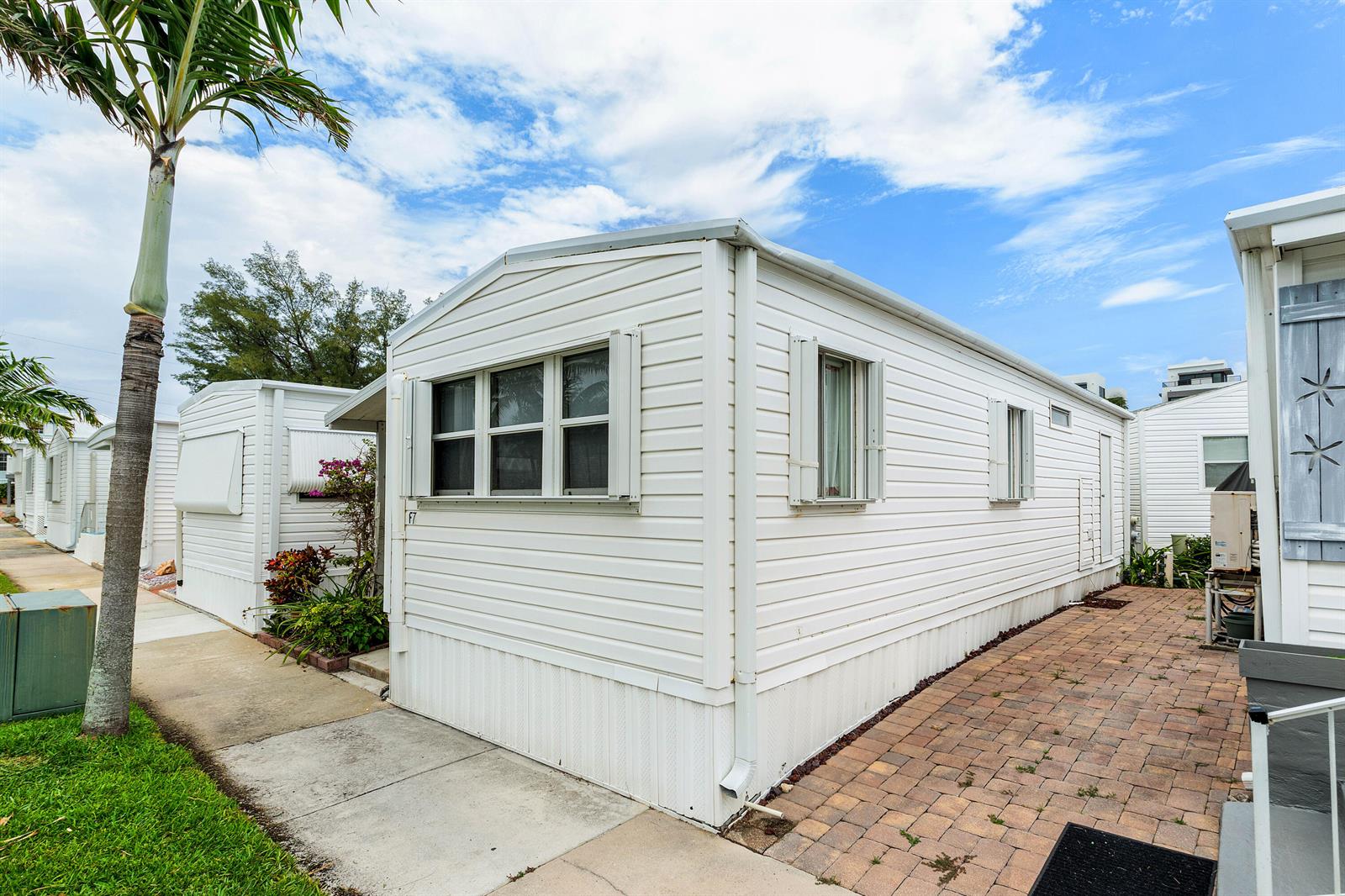 A white mobile home with vinyl siding and a brick patio under a blue sky — 7 Ruthmary Avenue # F, Briny Breezes FL 33435, BRINY BREEZES, FL