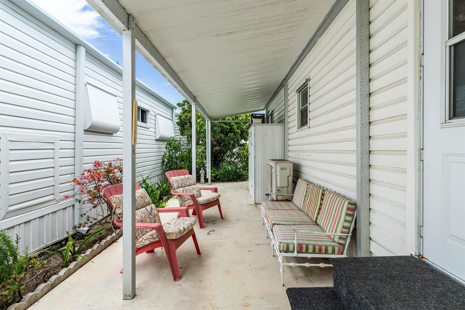 A covered concrete patio features two pink chairs and a striped bench seat — 7 Ruthmary Avenue # F, Briny Breezes FL 33435, BRINY BREEZES, FL