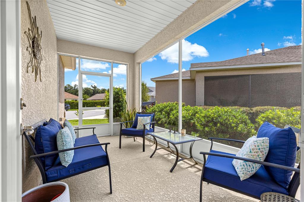 A screened-in patio features blue cushioned outdoor furniture, a glass-topped table, and concrete flooring — 8952 SW 78TH COURT, OCALA, FL