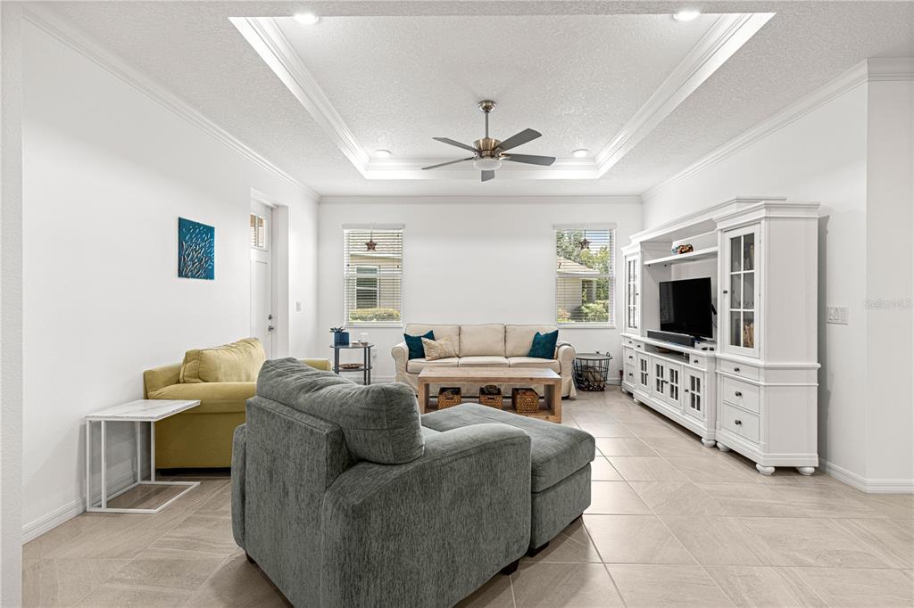 A living room features a tray ceiling, tile flooring, a white entertainment center, and neutral furniture — 8952 SW 78TH COURT, OCALA, FL