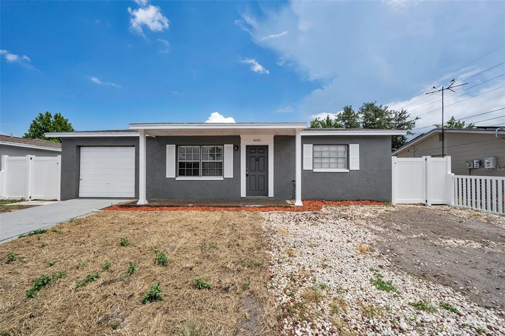 A single-story gray house with a white garage door, front porch, and white vinyl fencing — 8053 DEDHAM DRIVE, PORT RICHEY, FL