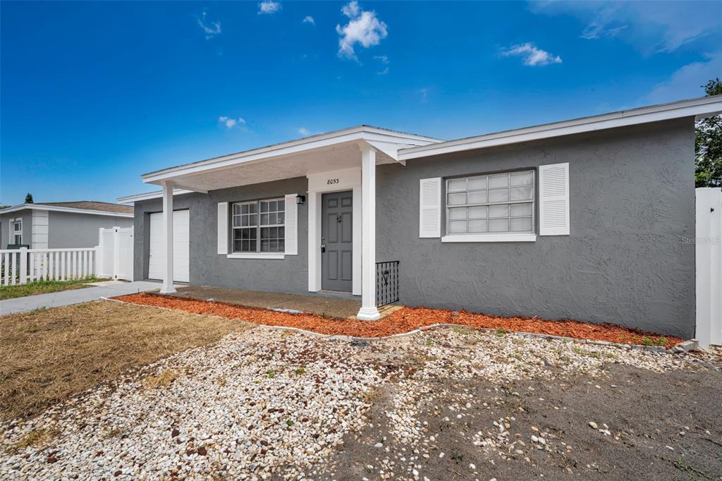 A single-story gray house with a covered porch, white trim, and a gravel front yard — 8053 DEDHAM DRIVE, PORT RICHEY, FL