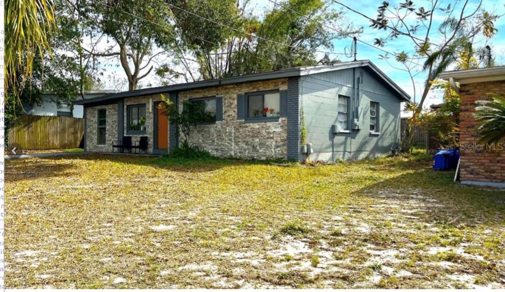 A single-story house with a stone facade, gray siding, and a large, grassy front yard — 7011 CONIFER DRIVE, TAMPA, FL