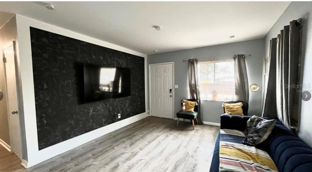 A living room features a dark textured accent wall with a mounted television and wood flooring — 7011 CONIFER DRIVE, TAMPA, FL