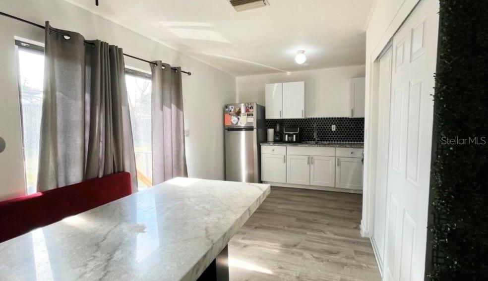 A kitchen features white cabinets, a black honeycomb backsplash, stainless steel appliances, and a dining area — 7011 CONIFER DRIVE, TAMPA, FL