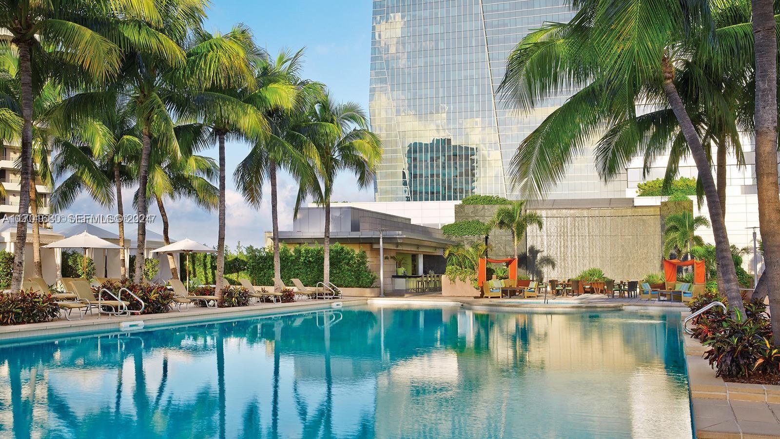 A swimming pool sits in front of a modern glass building surrounded by palm trees — 1435 Brickell Ave # 3307, Miami FL 33131, MIAMI, FL