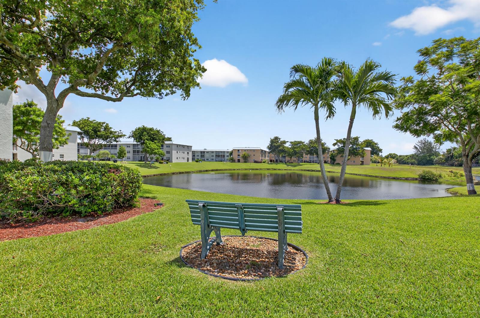 A green bench sits on a gravel patch overlooking a pond surrounded by apartment buildings — 9880 Marina Boulevard # 1509, Boca Raton FL 33428, BOCA RATON, FL