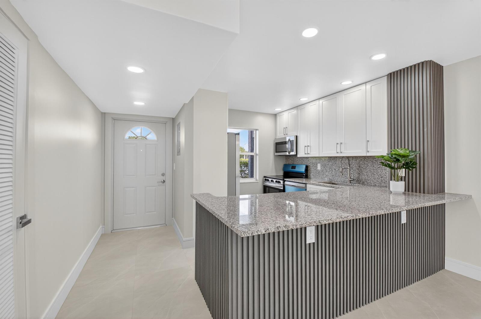 A kitchen with white cabinets, granite countertops, and a gray slatted breakfast bar — 9880 Marina Boulevard # 1509, Boca Raton FL 33428, BOCA RATON, FL