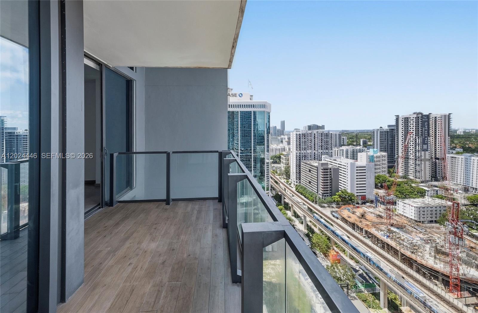A high-rise balcony features wood-look flooring, glass railings, and a view of city buildings — 88 SW 7th St # 2008, Miami FL 33130, MIAMI, FL