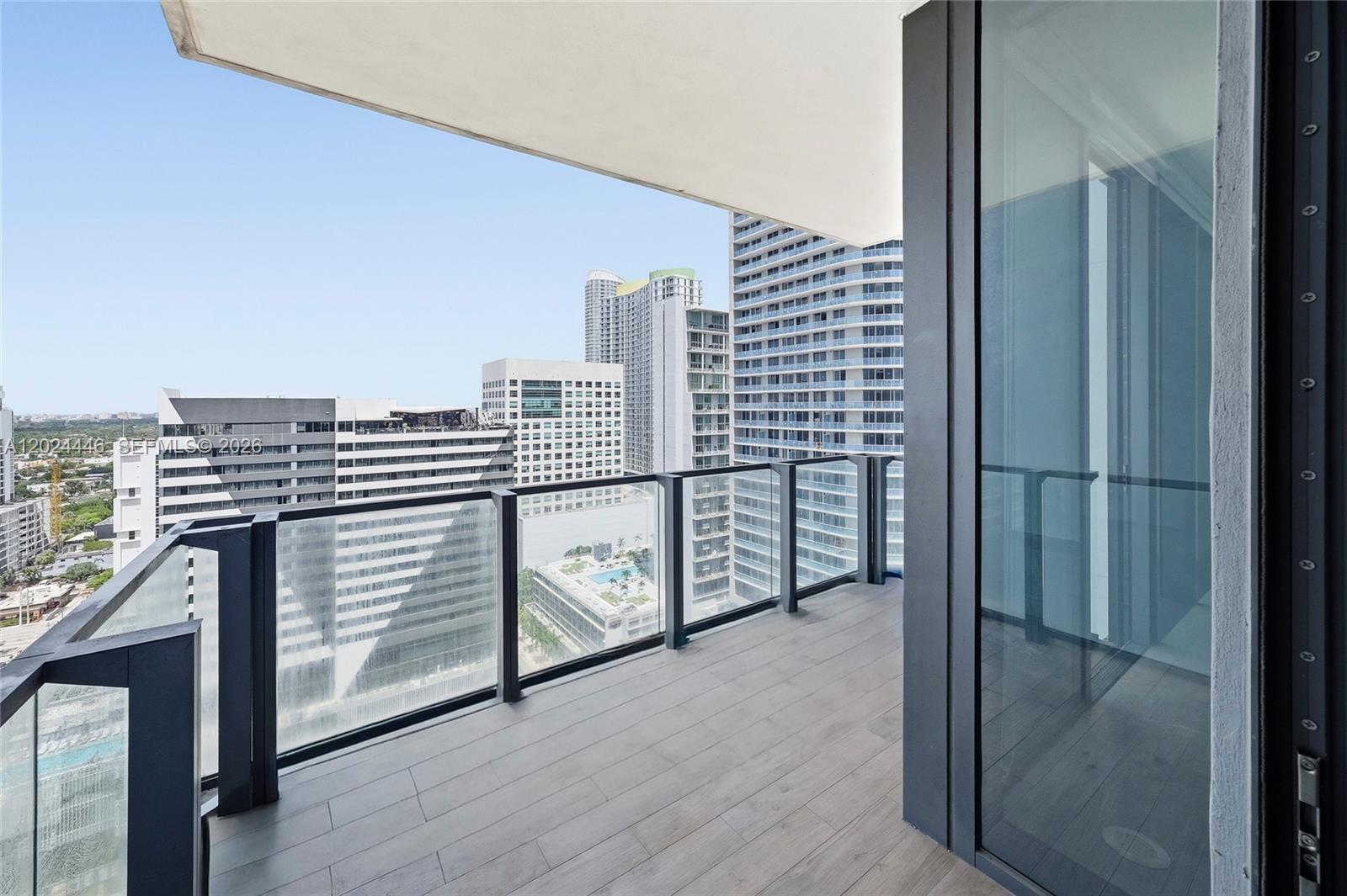 A balcony with wood-look flooring and a glass railing overlooks a dense urban cityscape — 88 SW 7th St # 2008, Miami FL 33130, MIAMI, FL