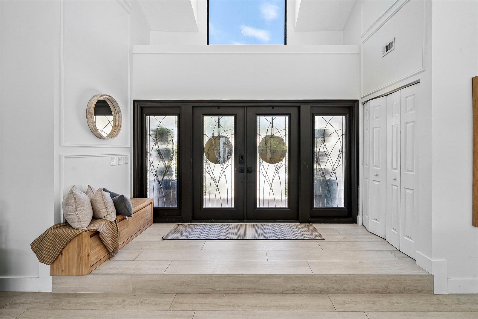 A bright entryway features a raised tiled floor, double front doors, and a wooden bench — 2707 Biarritz Drive, Palm Beach Gardens FL 33410, PALM BEACH GARDENS, FL
