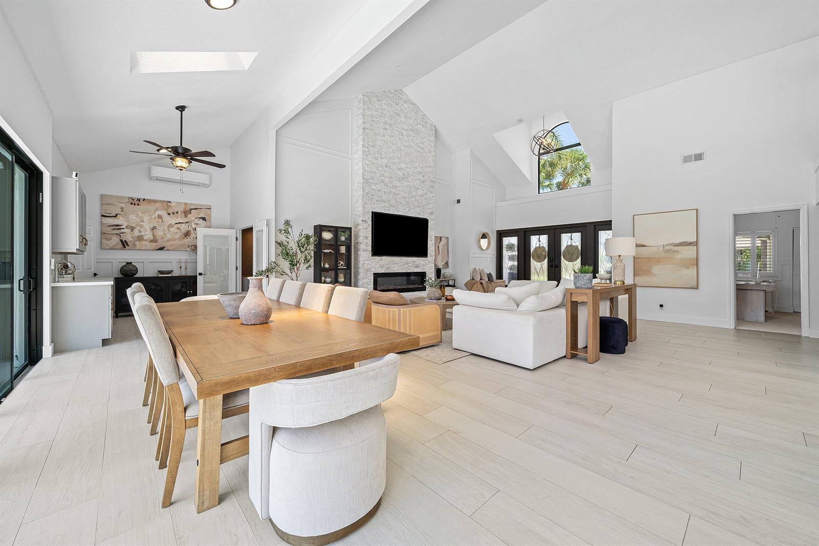 A bright, open-concept living and dining area features vaulted ceilings, a stone fireplace, and tile flooring — 2707 Biarritz Drive, Palm Beach Gardens FL 33410, PALM BEACH GARDENS, FL