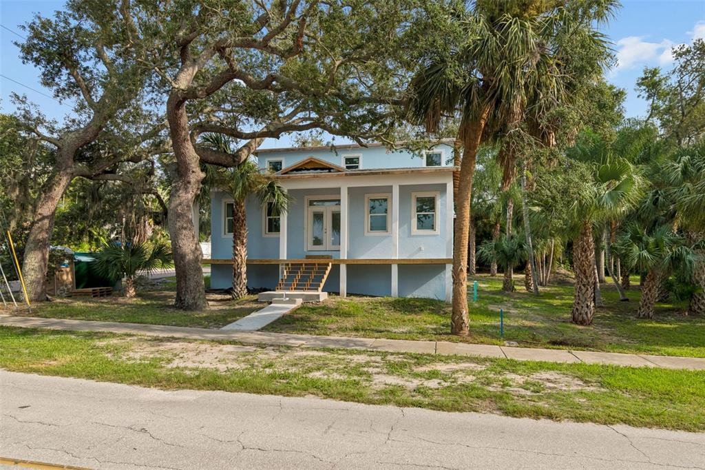 A light blue elevated house with a front porch and stairs sits among large trees — 383 GEORGIA AVENUE, CRYSTAL BEACH, FL