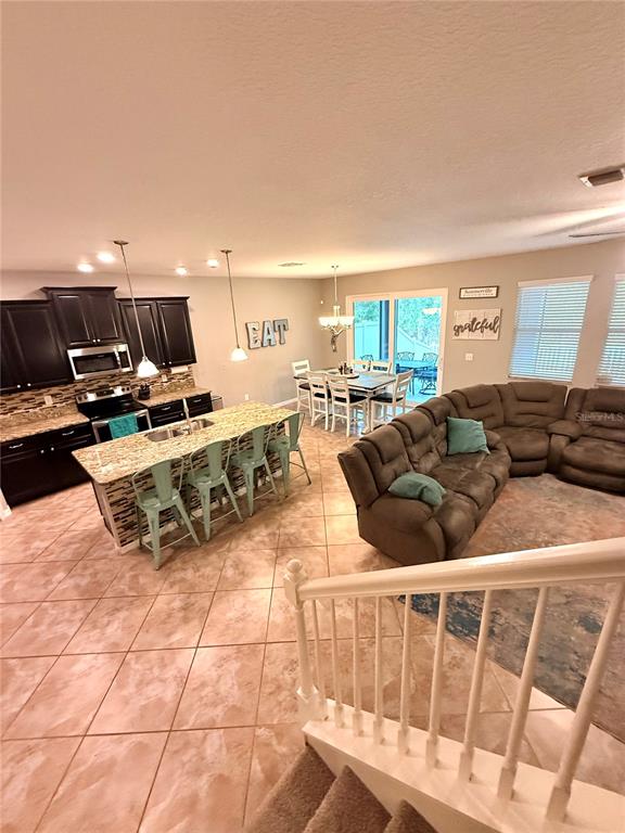 An open-concept kitchen and living area features dark cabinetry, a granite island, and tile flooring — 14250 BLUE DASHER DRIVE, RIVERVIEW, FL