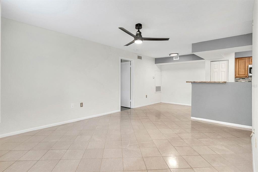 An open-concept living area features light tile flooring, a ceiling fan, and a kitchen pass-through — 3032 PARKWAY BOULEVARD UNIT 201, KISSIMMEE, FL