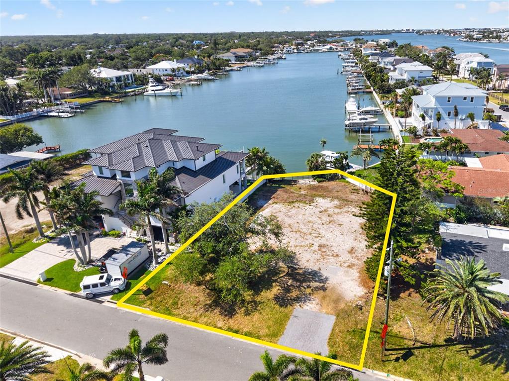 An aerial view shows a vacant waterfront lot outlined in yellow next to a large house — 909 OAKWOOD DRIVE, LARGO, FL