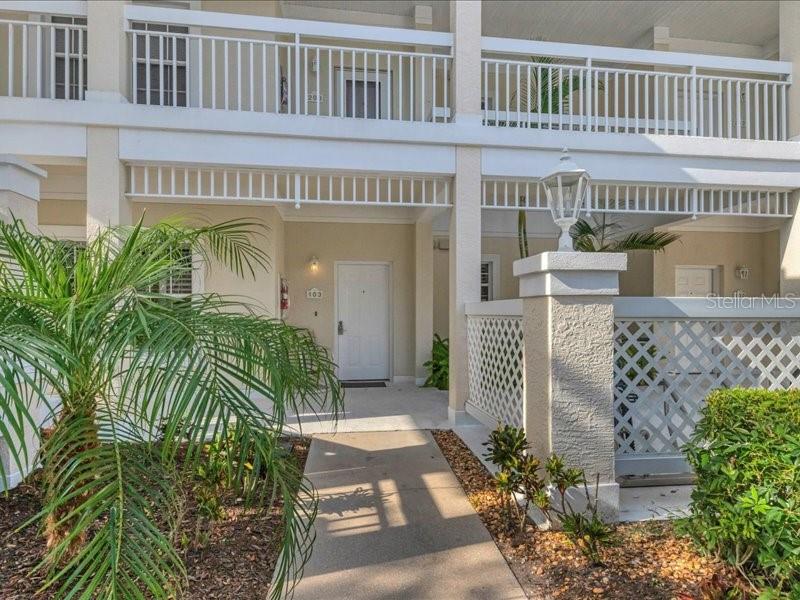A walkway leads to the white front door of a multi-story residential building with balconies — 3706 54TH DRIVE W UNIT 103, BRADENTON, FL