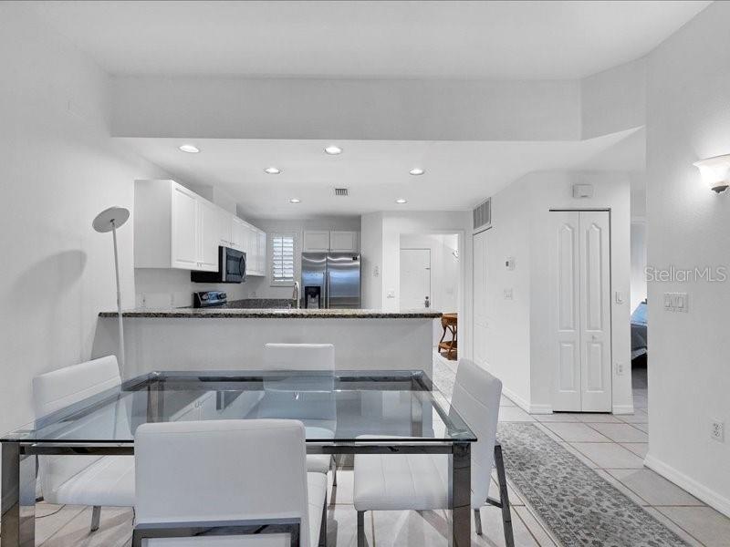 A dining area with a glass table and white chairs sits before an open kitchen — 3706 54TH DRIVE W UNIT 103, BRADENTON, FL