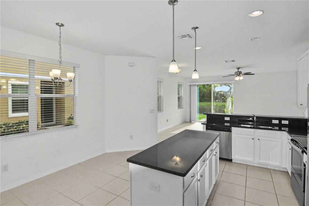 A kitchen features white cabinets, black countertops, a center island, and a dining area — 4240 GUMBO LIMBO DRIVE, ORLANDO, FL