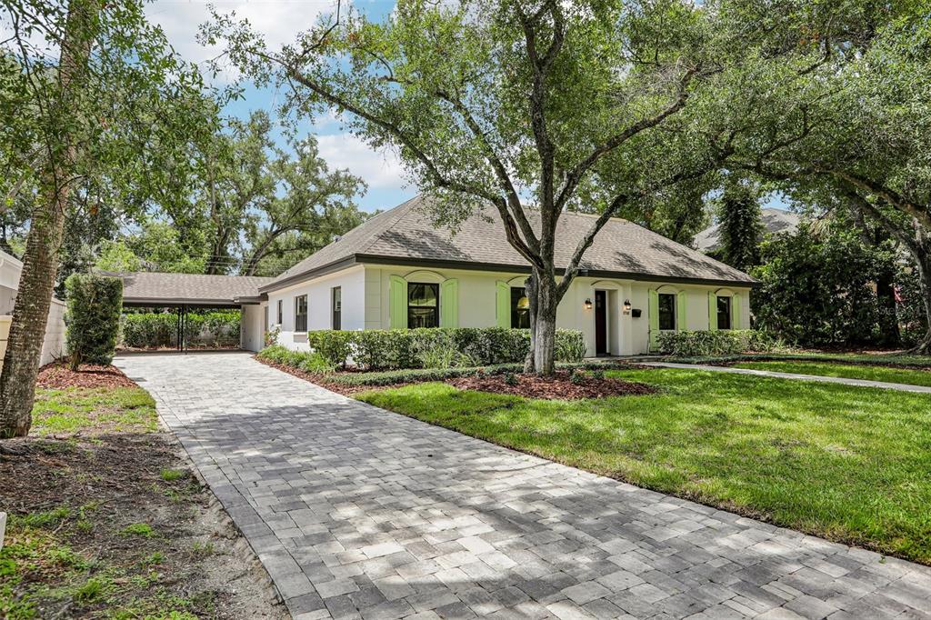 A single-story house with a paved driveway, carport, and light-colored exterior walls under large trees — 4708 W NEPTUNE STREET, TAMPA, FL
