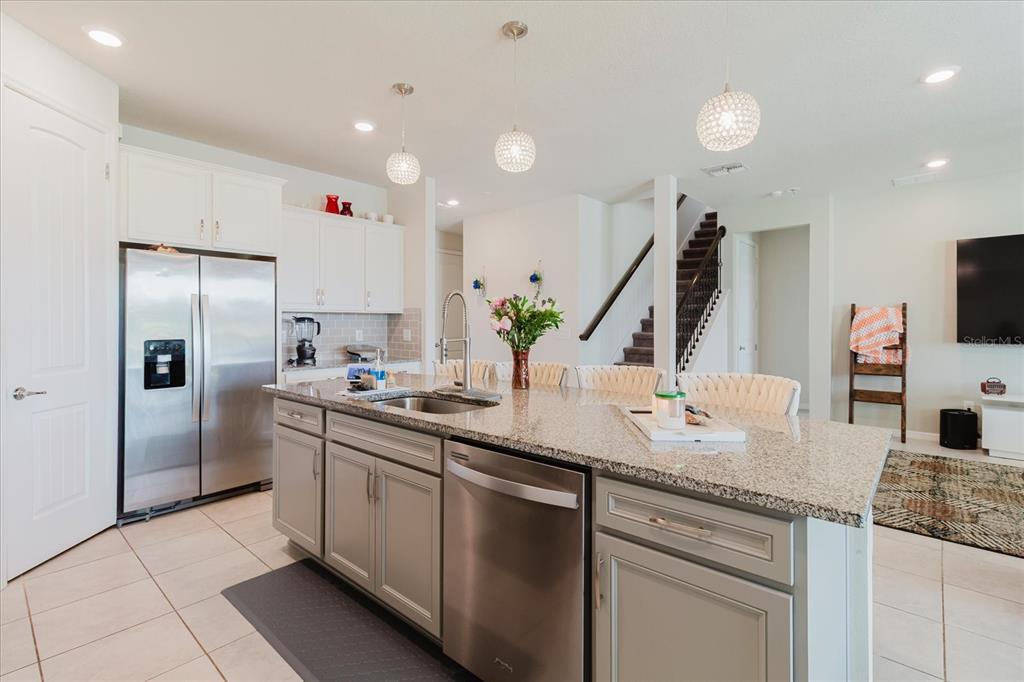 A kitchen island with a granite countertop and stainless steel dishwasher sits before white cabinets — 10307 WINE PRESS AVENUE, RIVERVIEW, FL
