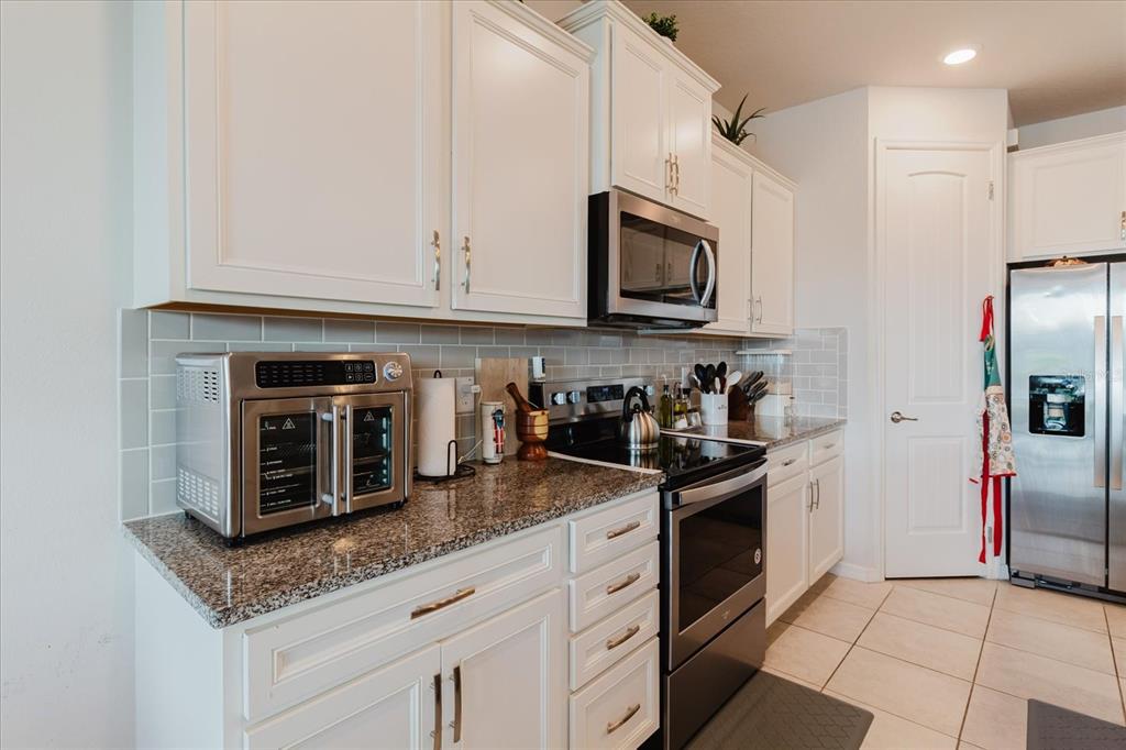 A kitchen features white cabinets, granite countertops, stainless steel appliances, and a subway tile backsplash — 10307 WINE PRESS AVENUE, RIVERVIEW, FL