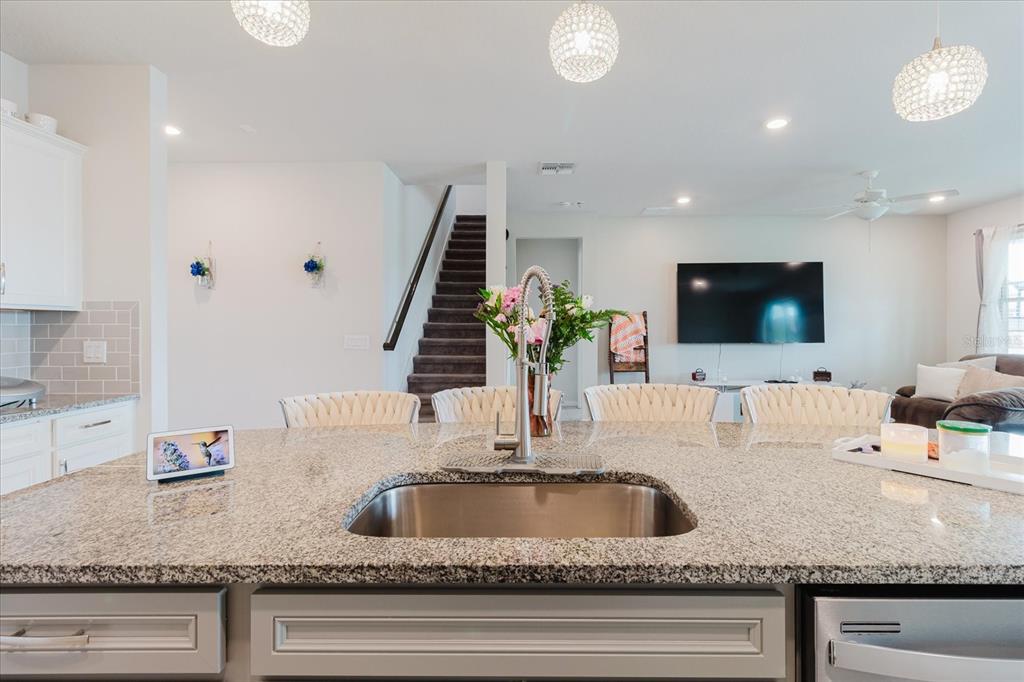 A kitchen island with a granite countertop and stainless steel sink faces a living area — 10307 WINE PRESS AVENUE, RIVERVIEW, FL