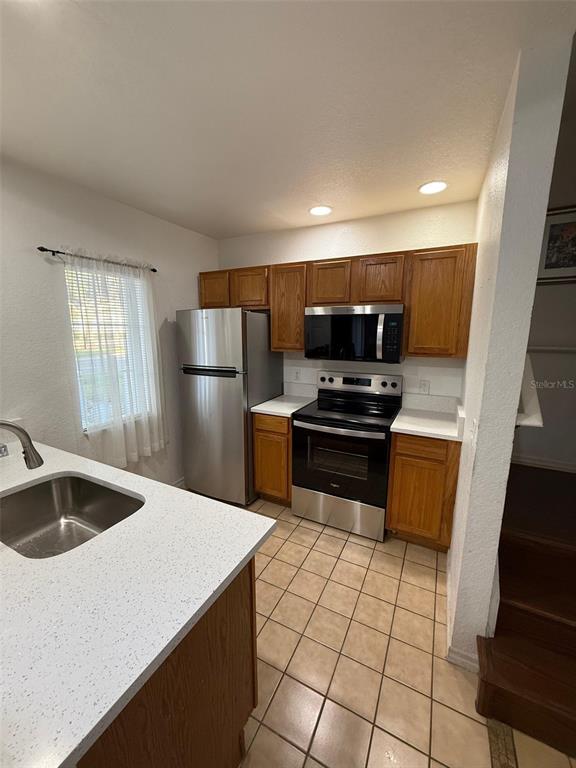 A kitchen features wood cabinets, stainless steel appliances, white countertops, and a tiled floor — 2250 SAN VITAL DRIVE UNIT 107, KISSIMMEE, FL