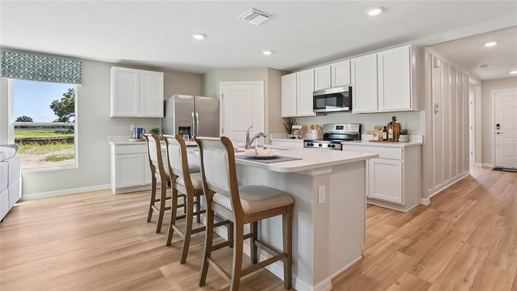 A bright kitchen features white cabinets, a central island with bar seating, and wood flooring — 11085 NW 167TH TERRACE, ALACHUA, FL