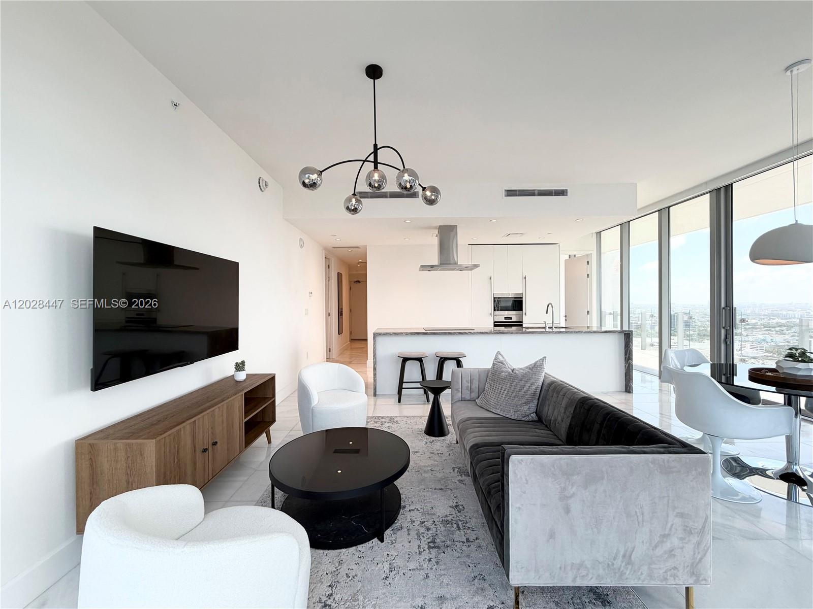 A modern open-concept living room and kitchen feature white walls, tile floors, and floor-to-ceiling windows — 700 NE 26th Ter # 3206, Miami FL 33137, MIAMI, FL