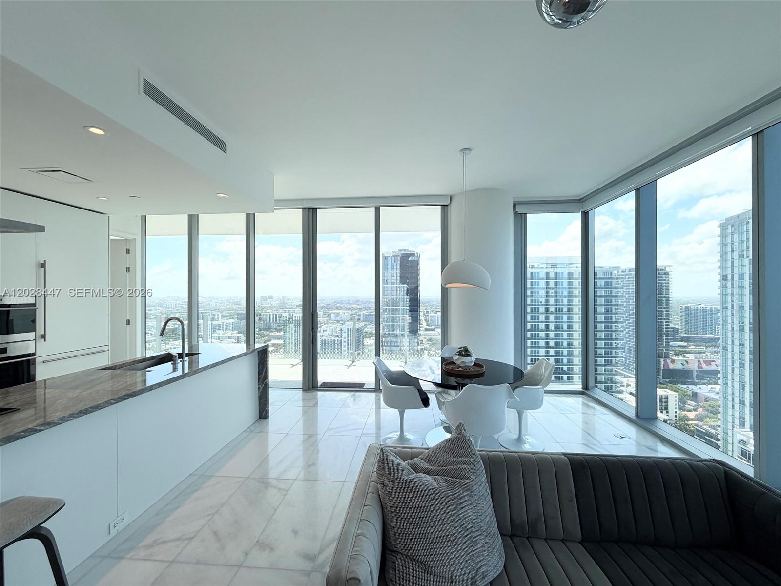 A modern kitchen and dining area feature floor-to-ceiling windows with expansive city views — 700 NE 26th Ter # 3206, Miami FL 33137, MIAMI, FL
