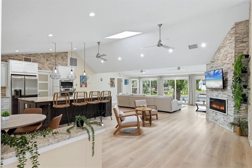 An open-concept living room and kitchen feature vaulted ceilings, stone accent walls, and wood flooring — 1232 NORTHPORT DRIVE, SARASOTA, FL