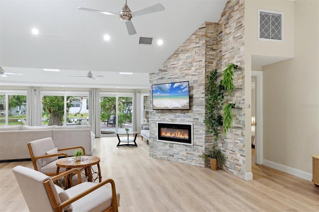A living room features a stone fireplace, a wall-mounted television, and large sliding glass doors — 1232 NORTHPORT DRIVE, SARASOTA, FL