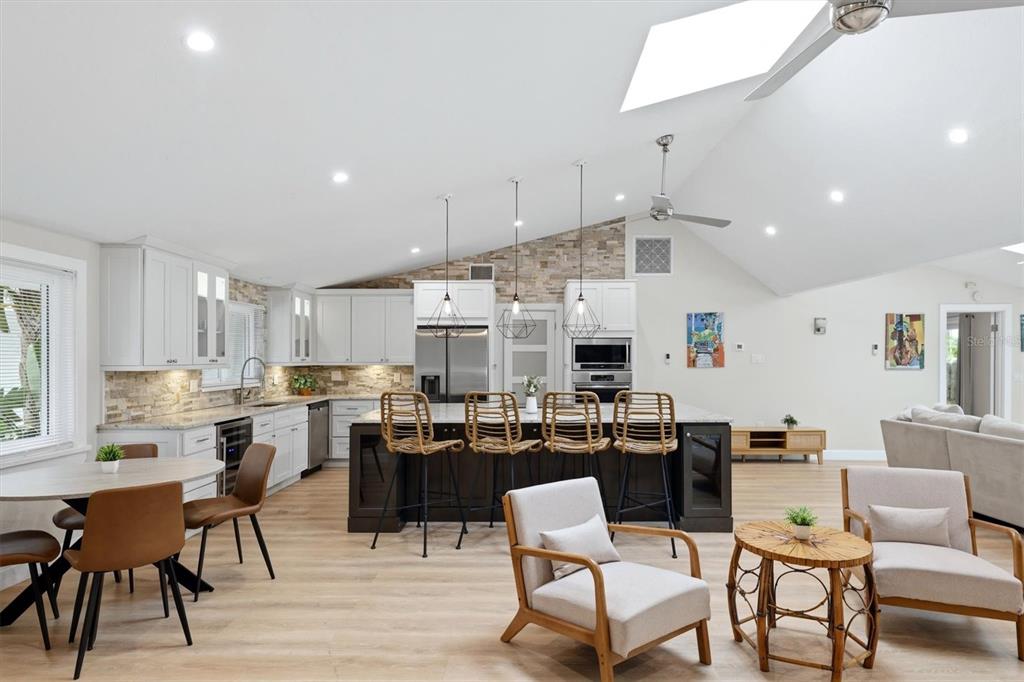 A bright, open-concept kitchen features white cabinetry, a dark island with bar seating, and vaulted ceilings — 1232 NORTHPORT DRIVE, SARASOTA, FL