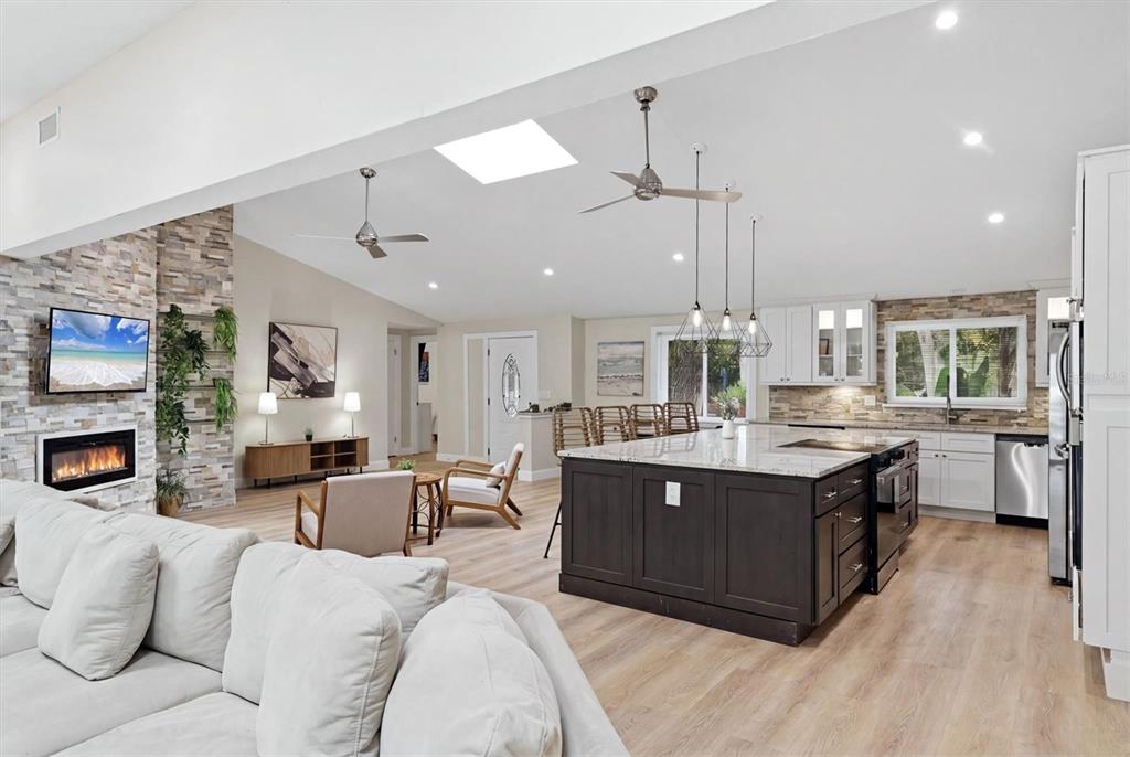 An open-concept living room and kitchen featuring a stone fireplace, island, and light wood flooring — 1232 NORTHPORT DRIVE, SARASOTA, FL