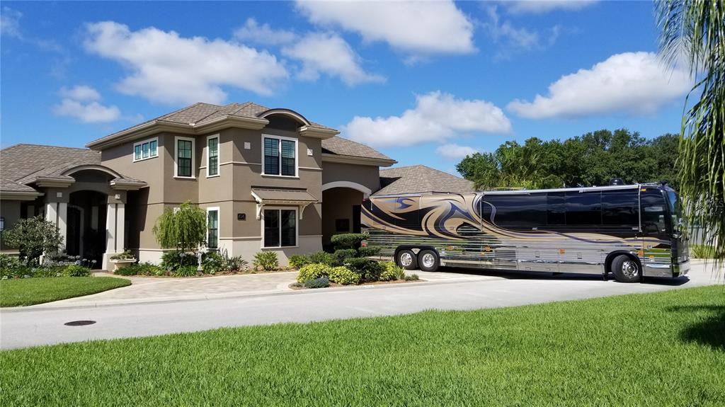A large luxury motorhome is parked in the driveway of a two-story suburban house — 414 MEANDERING WAY, POLK CITY, FL