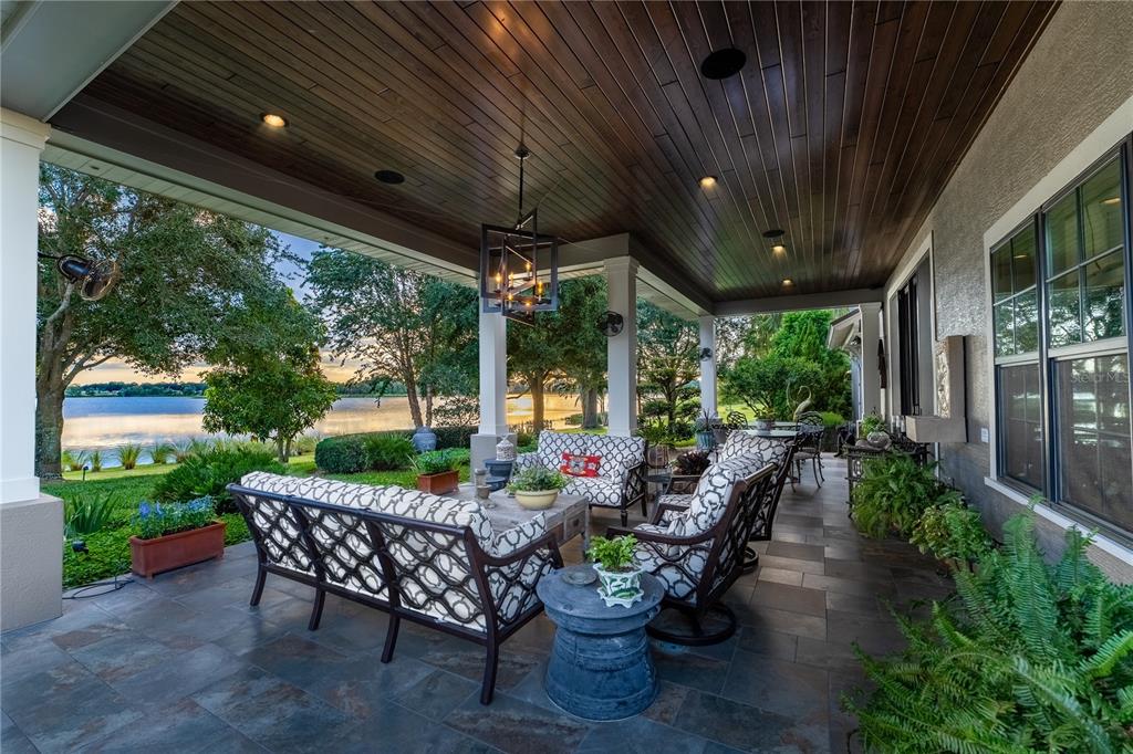 A covered patio features a dark wood ceiling, tile flooring, and outdoor furniture overlooking a lake — 414 MEANDERING WAY, POLK CITY, FL