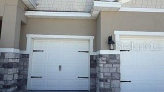 A two-car garage with white doors and stone veneer accents on the exterior — 1701 BULL HILL ROAD, KISSIMMEE, FL
